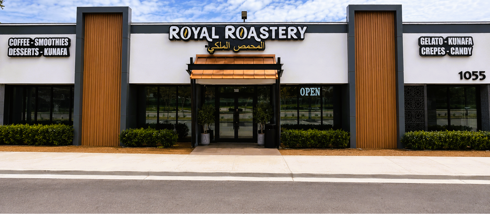 Front exterior of Royal Roastery storefront with large black and white signage, wood-toned vertical panels, glass windows, and a blue sky with clouds behind it.